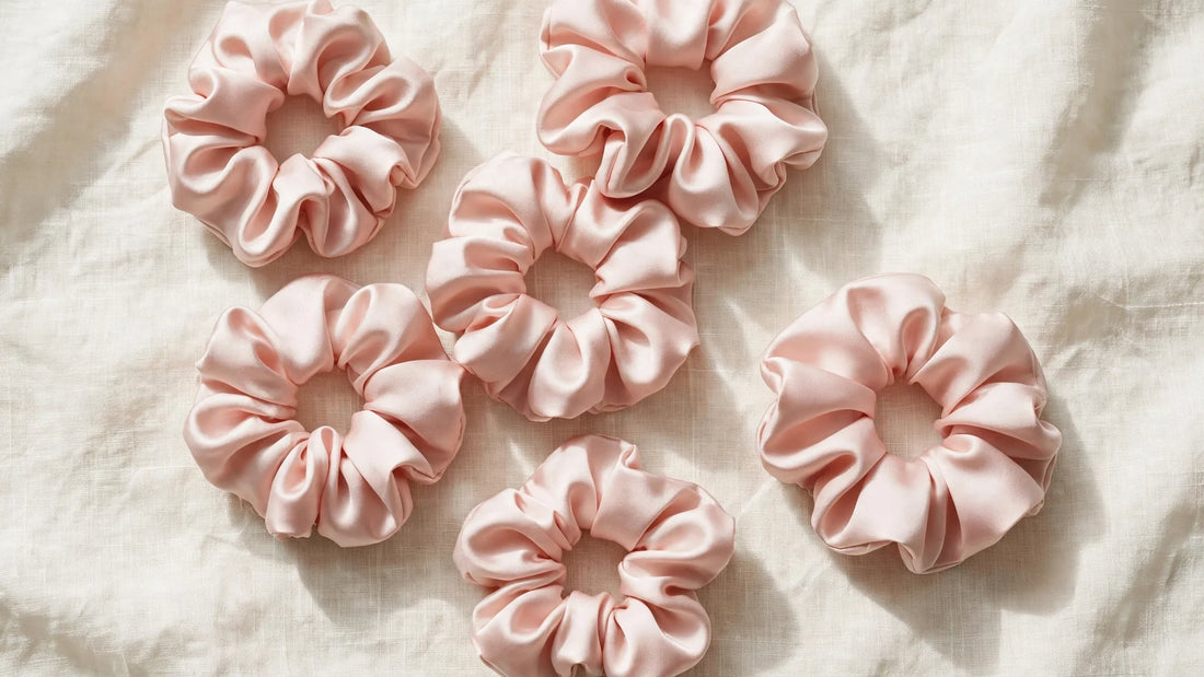 Mehrere blush-rosafarbene Seiden-Scrunchies elegant auf cremefarbenem Leinen arrangiert